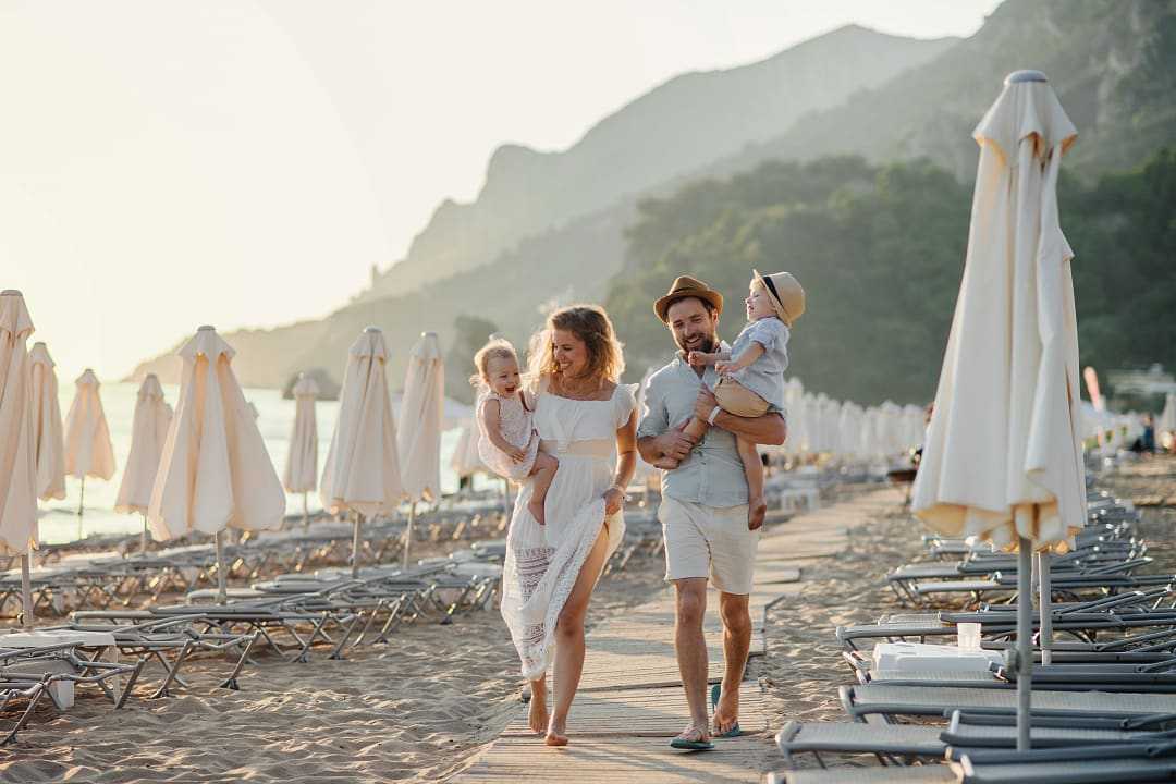 A young family with two toddler children walking on beach on summer vacation