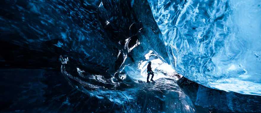 Mountain climber standing inside ice cave glacier Mountain climber standing inside ice cave glacier