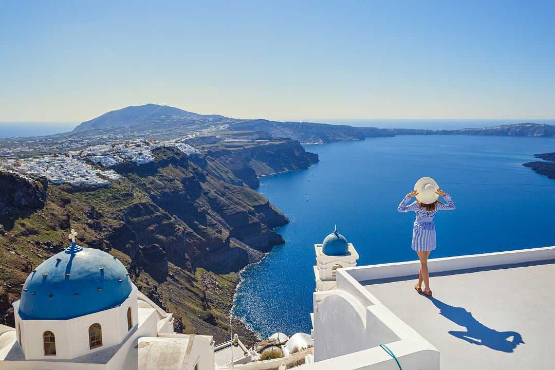 A woman admires Santorini’s breathtaking caldera and deep blue Aegean Sea. 