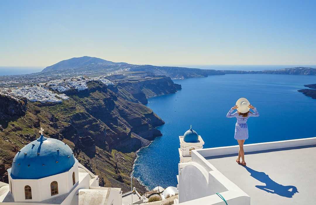 A woman admires Santorini’s breathtaking caldera and deep blue Aegean Sea. 
