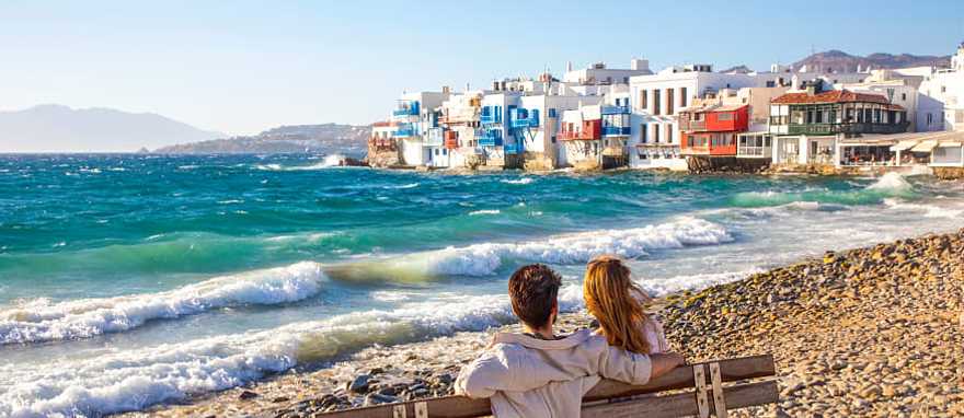 Romantic couple sitting on a beach bench near Little Venice in Mykonos, Greece