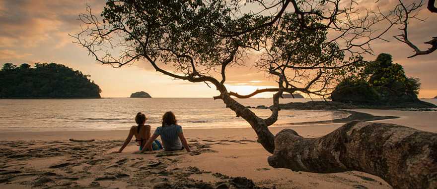Manuel Antonio, Costa Rica Couple sitting on the beach watching the sunset in Manuel Antonio National Park