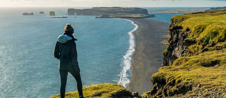 Hiker enjoying view of Reynisfjara and Dyrholaey Hiker enjoying view of Reynisfjara black sand beach and Dyrholaey in the distance