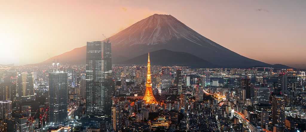 The Tokyo skyline at sunset, featuring the silhouette of Mount Fuji behind the glowing orange frame of the Tokyo Tower.