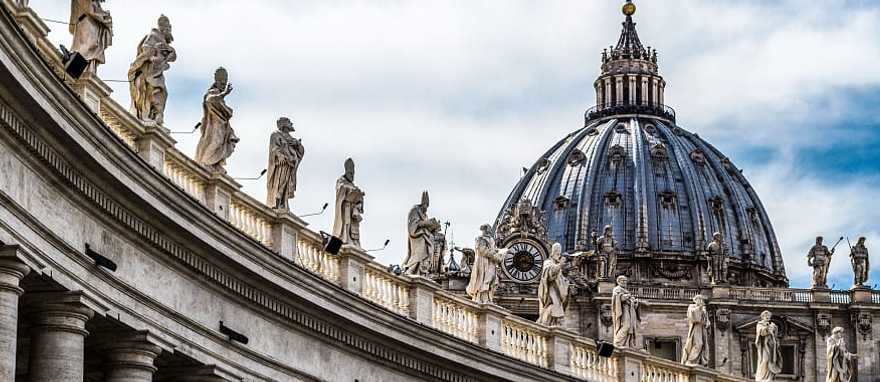 Intricate statues standing on a rooftop with the peak of St Peter's Basilica in the background. Intricate statues standing on a rooftop with the peak of St Peter's Basilica in the background.