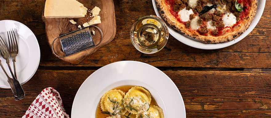 Classic Italian Foods Ravioli, pizza and wine on rustic restaurant table in Italy