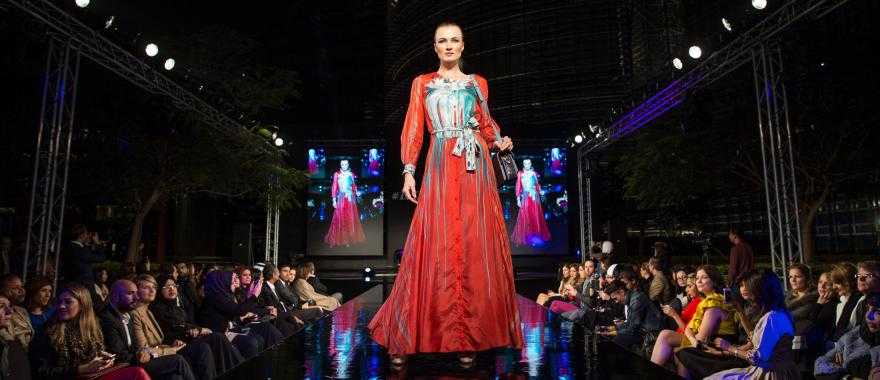 Runway model in a red dress at a fashion show. Credit: Ahmad Ardity