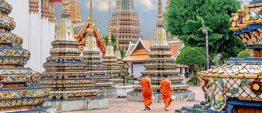 Two monks in colorful orange robes walking through Wat Pho Temple in Bangkok, Thailand