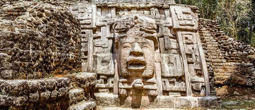 Ancient stone Mayan pre-columbian civilization pyramid with carved face in the forest, Lamanai archeological site, Orange Walk District, Belize Ancient stone Mayan pre-columbian civilization pyramid with carved face in the forest, Lamanai archeological site, Orange Walk District, Belize