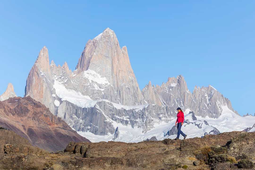 Hiker in red jacket walking with Mount Fitz Roy in Patagonia's stunning landscape as the backdrop